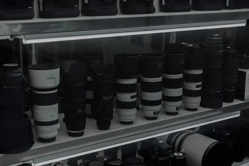 Multiple professional DSLR camera telephoto lenses neatly organized on shelves inside an electronic dry cabinet for humidity control.