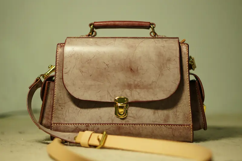 A structured pinkish-tan designer handbag with a distressed marble texture and a gold clasp lock, illustrating luxury leather protection