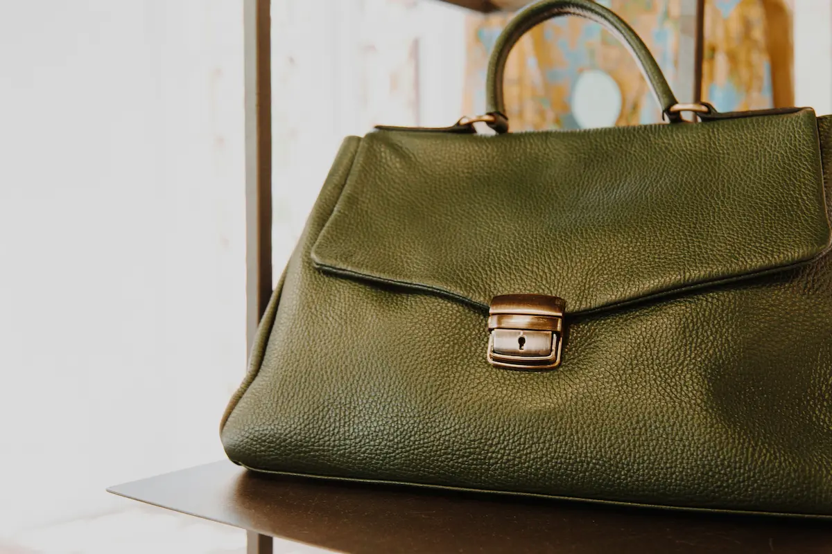 A luxury olive green designer handbag with a gold clasp displayed on a closet shelf, illustrating high-end bag care and storage