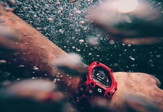 An underwater close-up of a person wearing a red Casio G-Shock water-resistant watch surrounded by air bubbles
