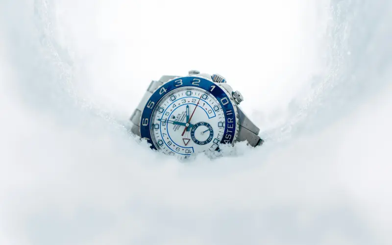 A luxury Rolex Yacht-Master II stainless steel watch with a blue ceramic bezel encased in a curved tunnel of white snow