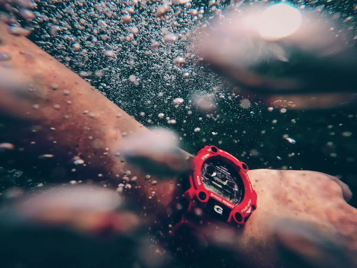 An underwater close-up of a person wearing a red Casio G-Shock water-resistant watch surrounded by air bubbles