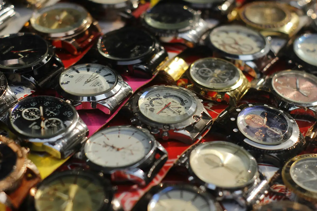 A high-angle close-up of dozens of various steel and gold-colored wristwatches displayed together at a street market