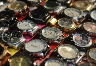 A high-angle close-up of dozens of various steel and gold-colored wristwatches displayed together at a street market