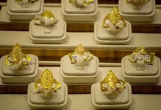 A rows of ornate gold rings with intricate filigree designs displayed on white stands inside a jewelry store showcase