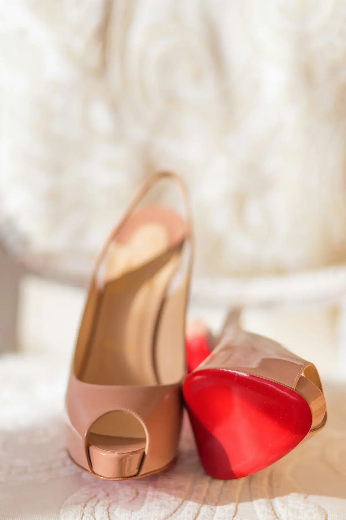 Pair of nude patent leather high heels displaying the iconic red lacquered sole, the signature of luxury footwear craftsmanship