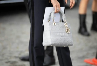 A close-up street style shot of a woman holding a grey Christian Dior Lady D-Lite handbag, showcasing its intricate geometric Cannage stitching pattern