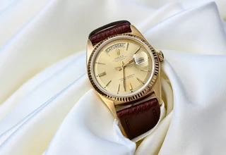 A vintage gold Rolex Day-Date mechanical watch with a brown leather strap resting on folds of elegant white silk fabric