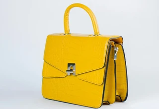 A vibrant yellow designer handbag with a faux crocodile leather texture, featuring a shiny silver clasp closure and metal hardware rings on a white background