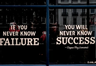 A moody, dramatic storefront window photograph showcasing a famous motivational quote by legend Sugar Ray Leonard: 'IF YOU NEVER KNOW FAILURE, YOU WILL NEVER KNOW SUCCESS'