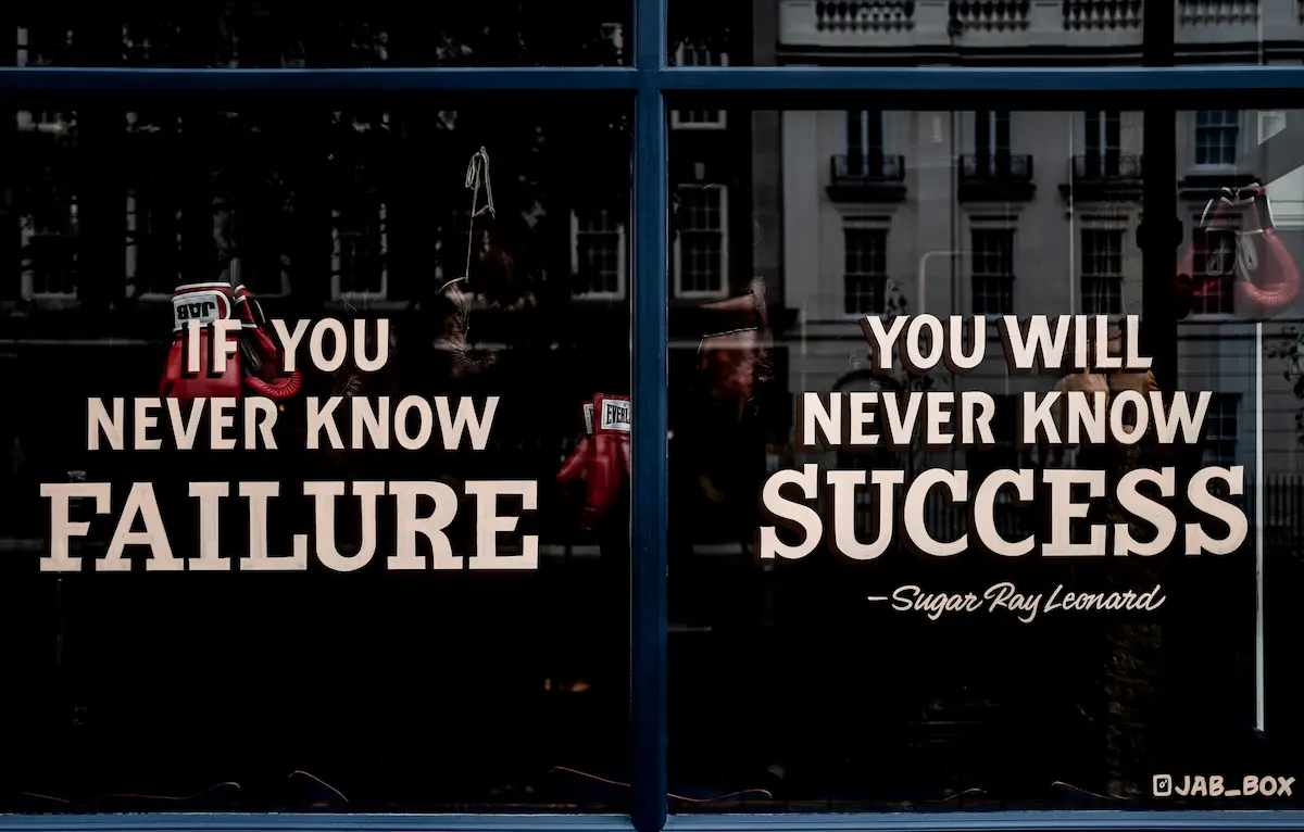 A moody, dramatic storefront window photograph showcasing a famous motivational quote by legend Sugar Ray Leonard: 'IF YOU NEVER KNOW FAILURE, YOU WILL NEVER KNOW SUCCESS'