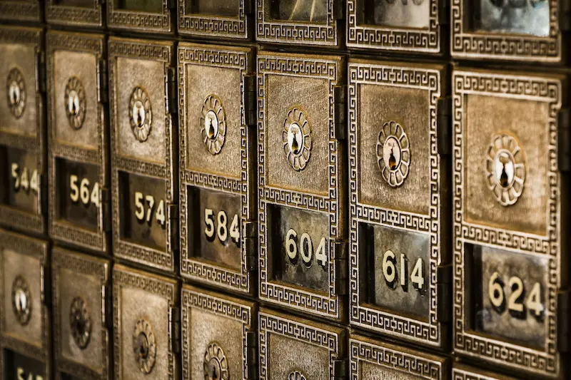 A row of antique metal bank safe deposit boxes with decorative borders, individual keyholes, and gold identification numbers like 584, 604, and 614