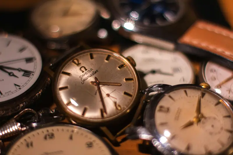 A close-up collection of vintage mechanical watches resting at various angles, featuring a vintage gold Omega Seamaster with a patinated dial in the center.