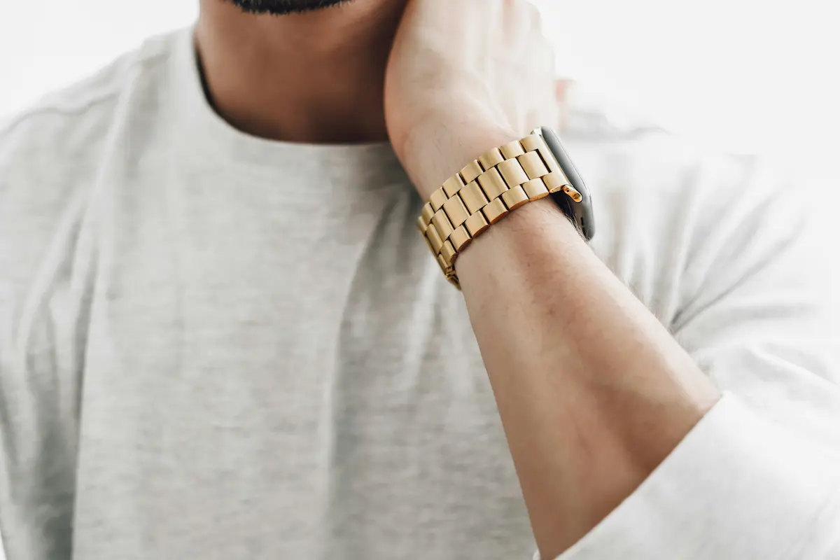 Close-up of a man wearing a smartwatch with a gold-toned case and matching gold link bracelet on his wrist