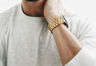 Close-up of a man wearing a smartwatch with a gold-toned case and matching gold link bracelet on his wrist