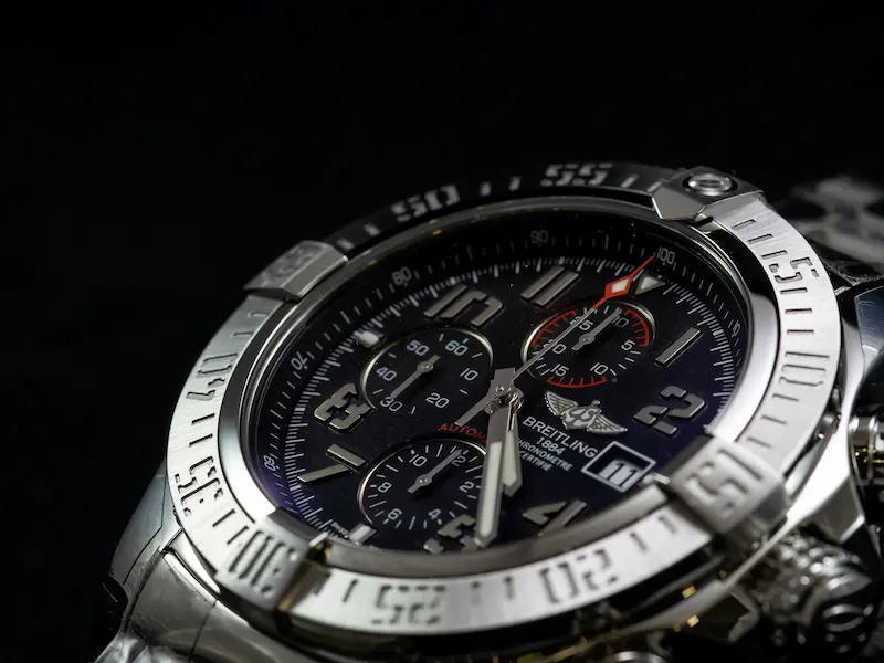 Macro close-up of a Breitling chronograph watch highlighting its stainless steel unidirectional rotating bezel with minute markers