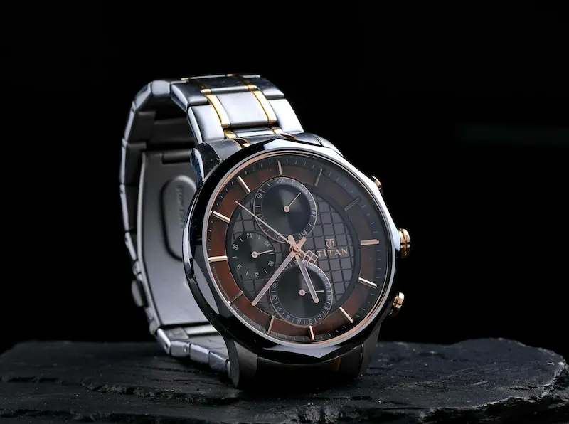 A two-tone Titan multi-function watch with a smooth fixed bezel resting on a dark slate stone surface