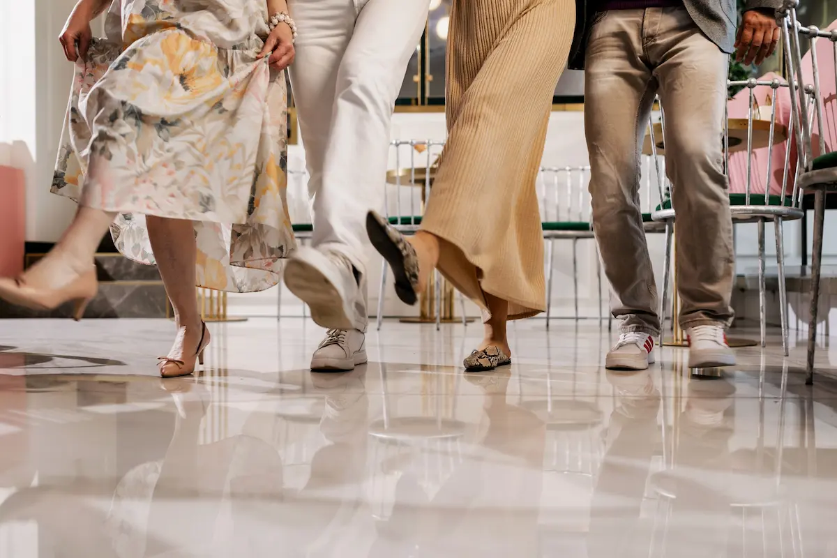 Lower body shot of four stylish people wearing quiet luxury footwear, including nude heels, white leather sneakers, and snakeskin patterned mules