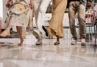 Lower body shot of four stylish people wearing quiet luxury footwear, including nude heels, white leather sneakers, and snakeskin patterned mules