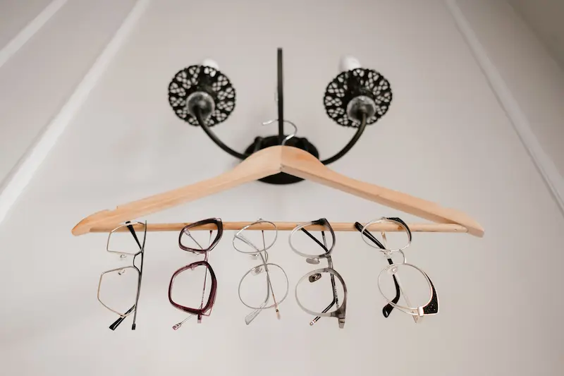 A row of various designer eyeglass frames hanging on a wooden hanger against a neutral background for quality inspection
