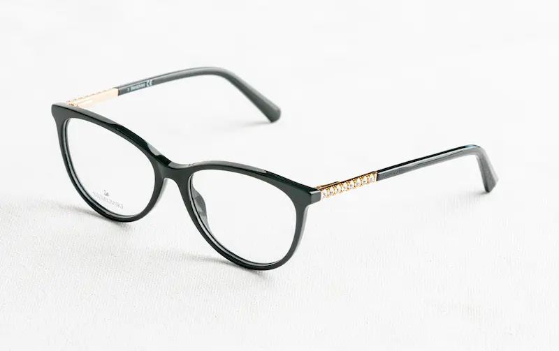A pair of black Swarovski luxury eyeglasses with crystal-embellished temples and authentic brand logo print on the demo lens