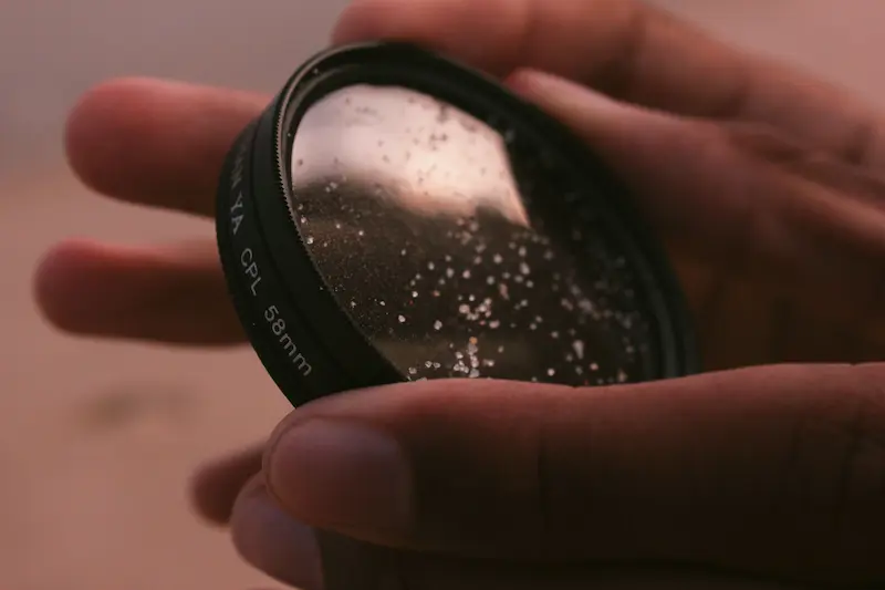 Close-up of a person holding a 58mm CPL camera lens filter to inspect surface dust, spots, and potential fungus contamination
