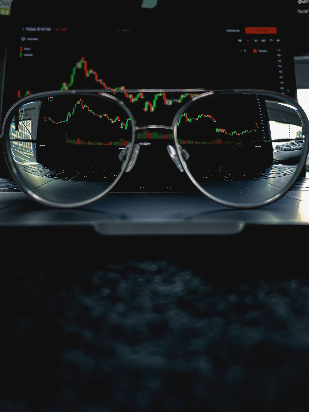 Investor's glasses reflecting financial market candlestick charts on a trading screen, representing the sophisticated analysis required for luxury goods ETF portfolio management