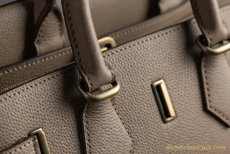 Close-up detail of premium pebbled calfskin leather and matte gold hardware on an unbranded quiet luxury handbag for 2026 fashion trends.