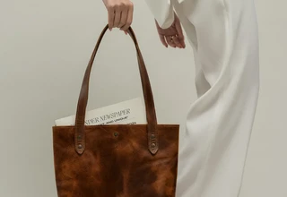 Woman in monochromatic white outfit carrying an unbranded brown leather tote bag, embodying the quiet luxury aesthetic where material quality and understated elegance replace conspicuous branding