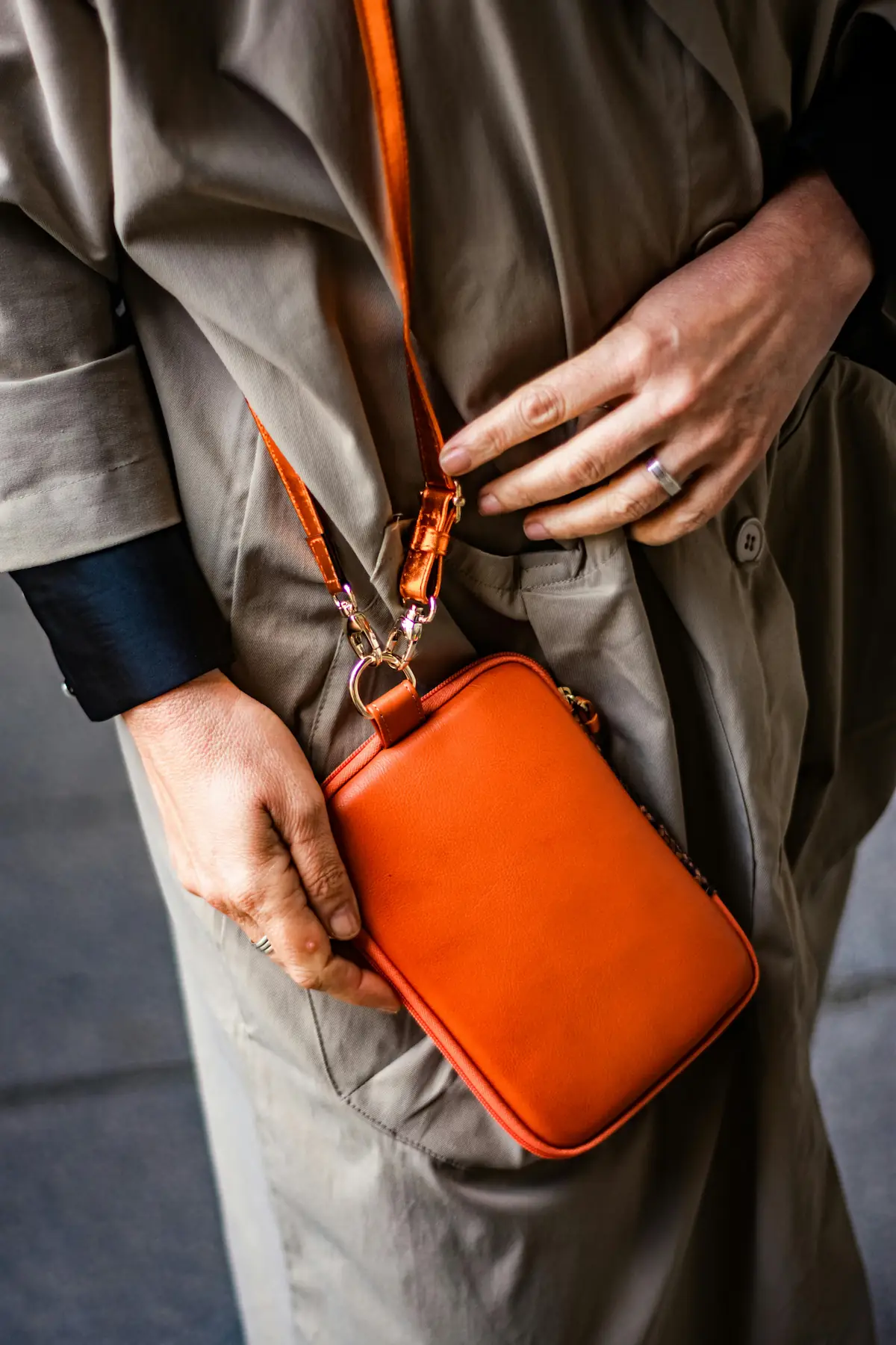 Person holding a pristine orange leather handbag against a neutral trench coat, representing the Hermès signature color and the investment-grade luxury asset class that has historically outperformed the S&P 500