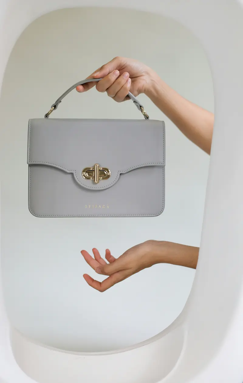 Hand holding luxury leather handbag showing gold hardware detail for authentication