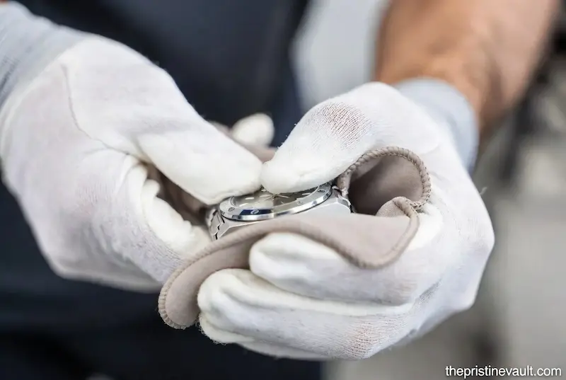 Close-up of a specialist polishing a stainless steel watch bezel with a microfiber cloth.