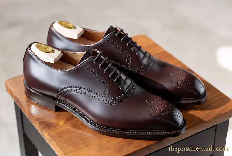 A pair of polished burgundy Allen Edmonds oxford shoes on a wooden stand, perfectly maintained with cedar wood shoe trees to preserve the leather shape and prevent creases.
