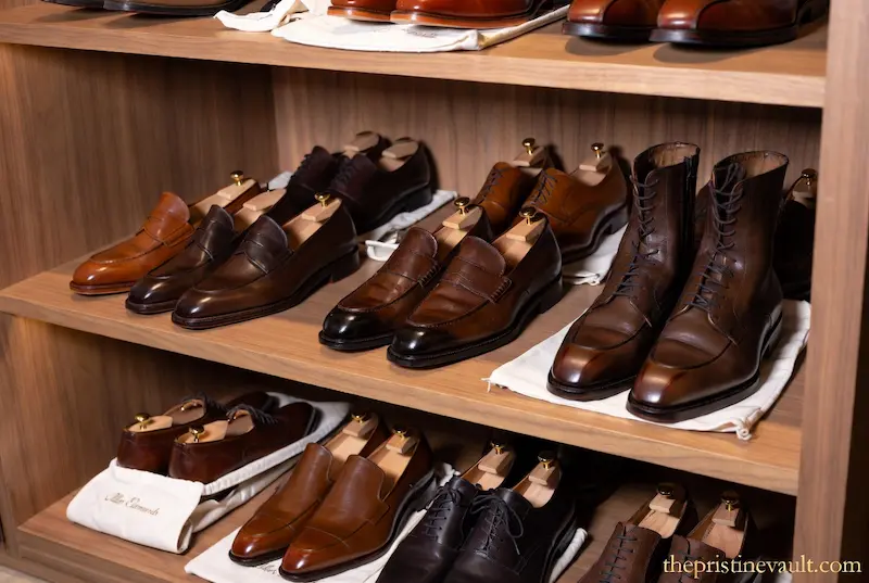 A luxury shoe collection featuring various Allen Edmonds loafers and boots organized on wooden shelves, all maintained with professional cedar shoe trees.
