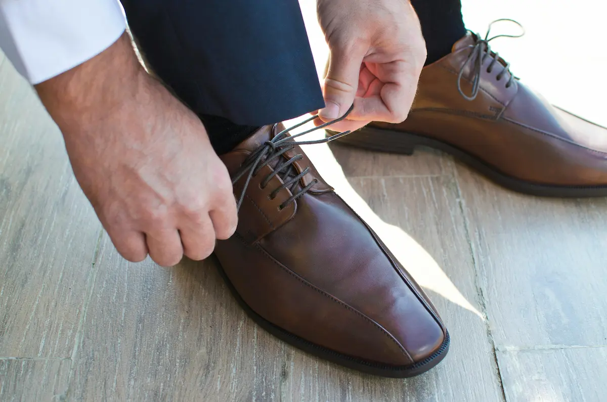 Man putting on premium brown leather dress shoes representing Allen Edmonds quality footwear that requires cedar shoe trees for long-term shape preservation