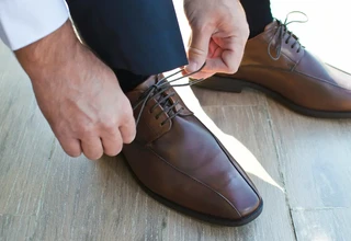 Man putting on premium brown leather dress shoes representing Allen Edmonds quality footwear that requires cedar shoe trees for long-term shape preservation