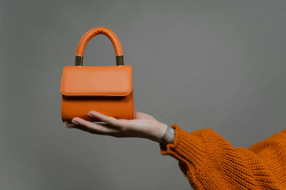 Orange leather luxury handbag held in hand showing smooth leather surface that requires proper conditioning with safe products to preserve Hermès-quality leather