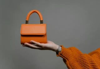 Orange leather luxury handbag held in hand showing smooth leather surface that requires proper conditioning with safe products to preserve Hermès-quality leather