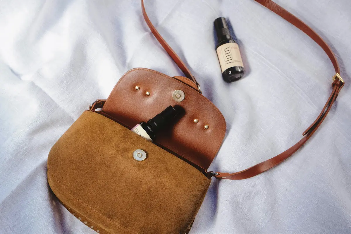 Tan suede and leather crossbody purse on natural linen background showing different leather textures that require gentle natural cleaning methods