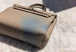 A light beige luxury leather Kelly bag with a visible blue denim color transfer stain on the side, demonstrating a leather care problem.