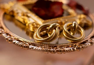Gold jewelry pieces including twisted rings displayed on an ornate gold mirror tray, representing fine gold accessories that require proper tarnish removal and home cleaning techniques to restore their natural brilliance