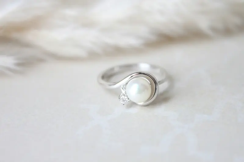 Elegant pearl ring set in sterling silver with a small diamond accent displayed on a soft white surface, representing the type of delicate pearl jewelry that requires gentle cleaning methods to preserve the nacre and natural luster