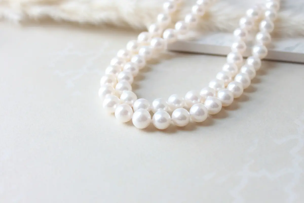 Lustrous white pearl necklace displayed on a clean cream surface showing the natural iridescent glow that proper gentle cleaning techniques help preserve without damaging the delicate nacre