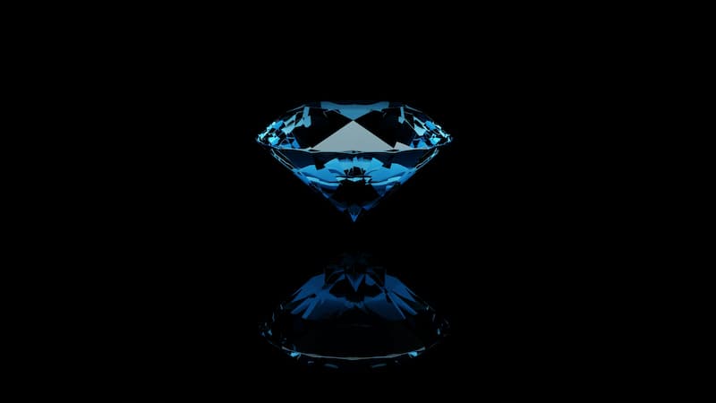A sparkling blue diamond with its reflection on a dark black surface, representing luxury diamond jewelry storage