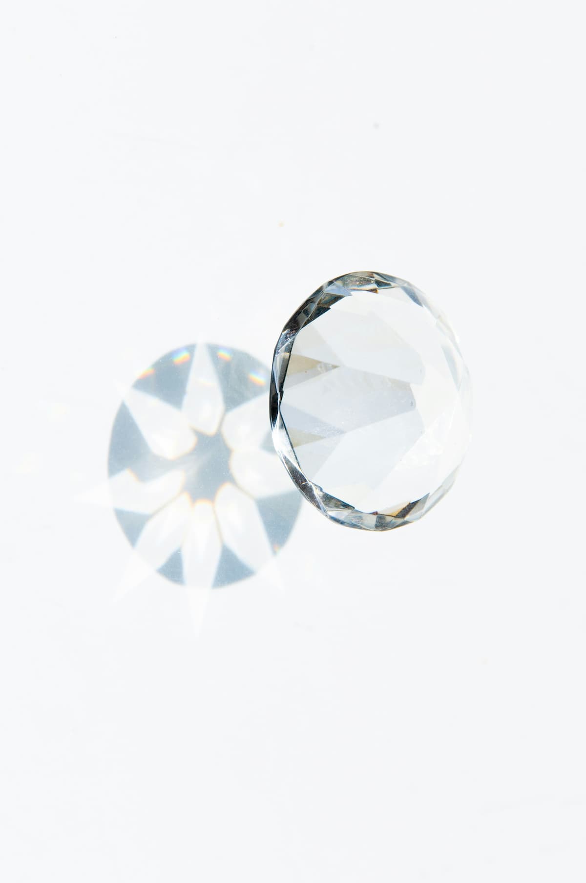 A round brilliant-cut diamond lying on a white surface, casting a sparkling light reflection beneath it