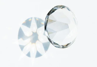 A round brilliant-cut diamond lying on a white surface, casting a sparkling light reflection beneath it