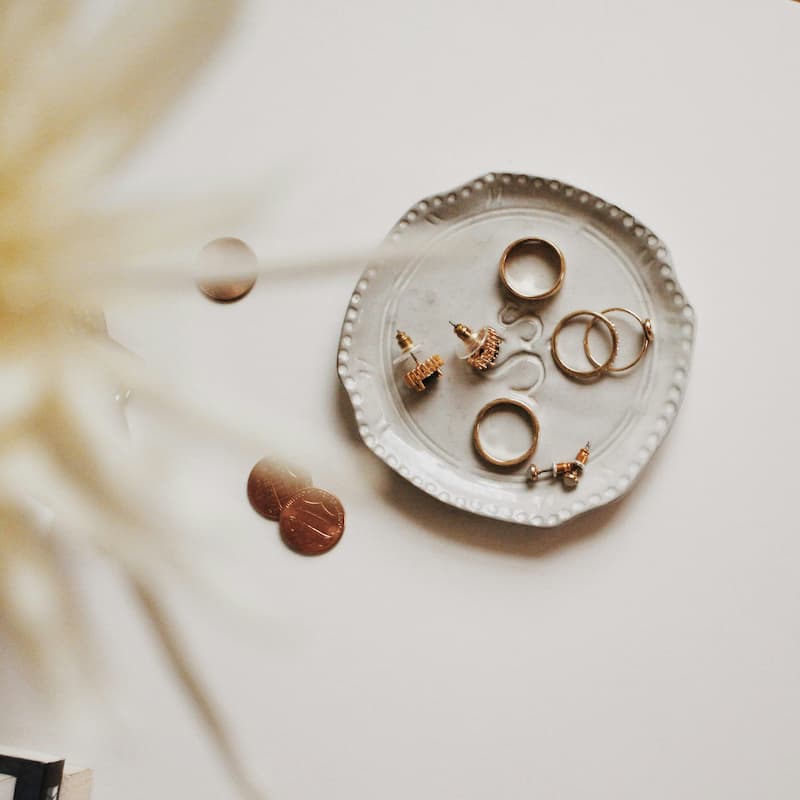 Gold rings and earrings neatly arranged on a small decorative white ceramic tray, showing proper jewelry storage organization