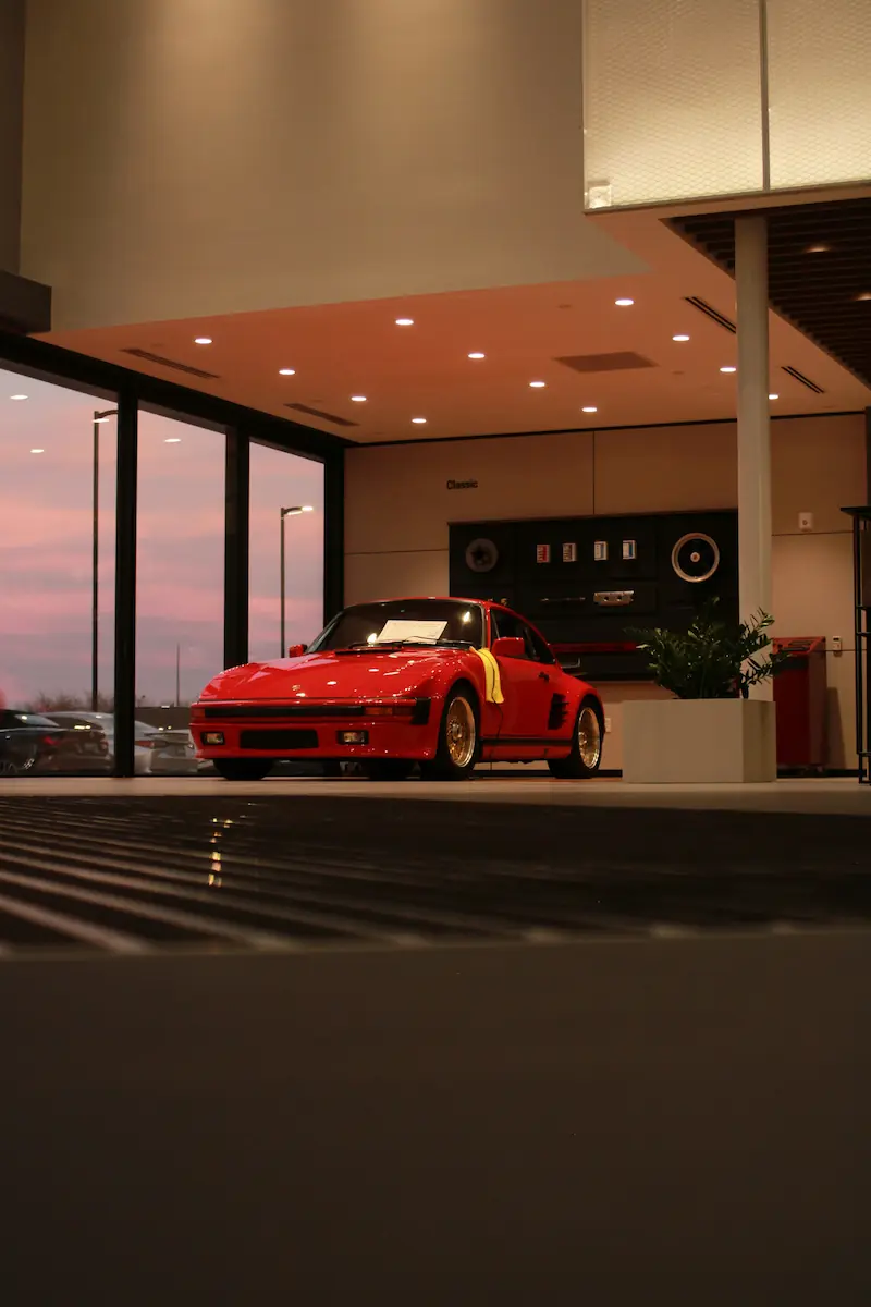 A classic red Porsche 930 Turbo displayed inside a luxury car showroom at dusk, representing high-value luxury assets in an ETF portfolio