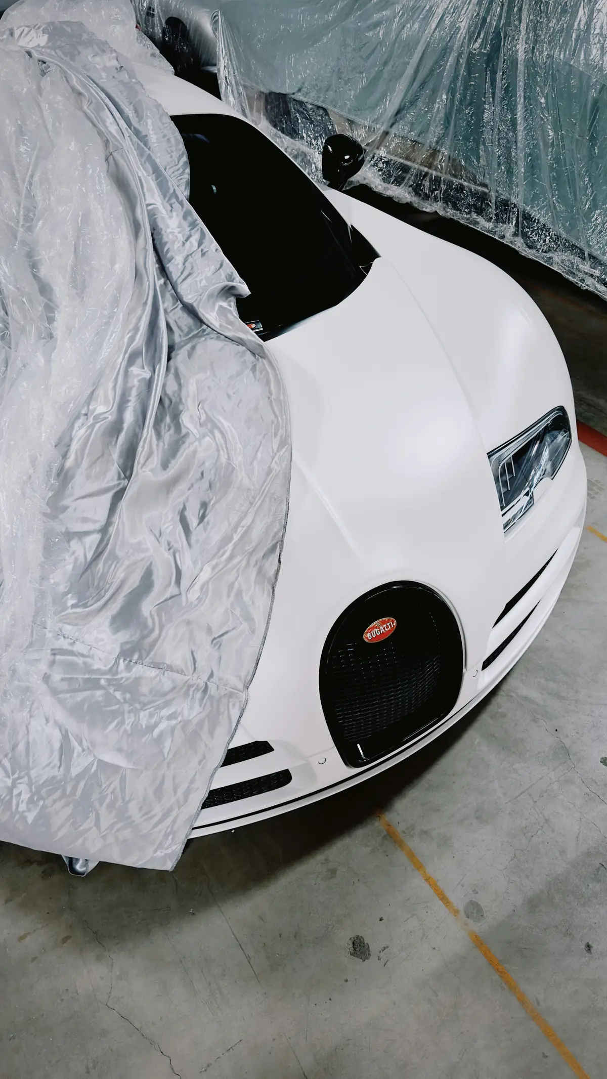 A white Bugatti Veyron supercar partially covered in a garage, representing high-value luxury goods and premium assets