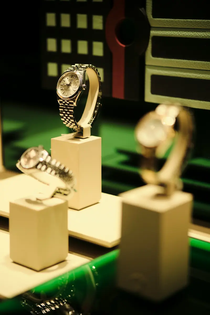 Luxury watches displayed on pedestals in an upscale boutique showcase, representing premium luxury goods investment